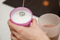 Woman using milk frother device in pitcher. Milk frother. Milk and coffee latte in glasses. In the kitchen.