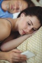 Woman using mobile phone while man sleeping on bed Royalty Free Stock Photo