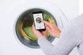 Woman Using Mobile Phone To Operate Washing Machine