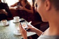 Woman Using Mobile Phone To Take Picture Of Drink In Coffee Shop To Post On Social Media