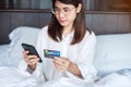 Woman using mobile smart phone and credit card for online shopping while making order on bed in morning at home. technology, Royalty Free Stock Photo