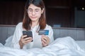 Woman using mobile smart phone and credit card for online shopping while making order on bed in morning at home. technology, Royalty Free Stock Photo