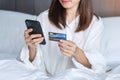 Woman using mobile smart phone and credit card for online shopping while making order on bed in morning at home. technology, Royalty Free Stock Photo