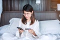 Woman using mobile smart phone and credit card for online shopping while making order on bed in morning at home. technology, Royalty Free Stock Photo