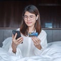 Woman using mobile smart phone and credit card for online shopping while making order on bed in morning at home. technology, Royalty Free Stock Photo