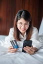 Woman using mobile smart phone and credit card for online shopping while making order on bed in morning at home. technology, Royalty Free Stock Photo