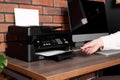 Woman using modern printer at wooden desk in home, closeup Royalty Free Stock Photo