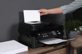 Woman using modern printer at wooden desk in home, closeup Royalty Free Stock Photo