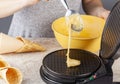 A woman is using a non stick electrical waffle cone maker to make homemade ice cream cones