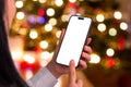 Woman using phone mockup near a sparkling Christmas tree