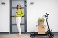 Woman with phone, electric scooter and packages going home