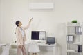 Woman using remote control to switch wall air conditioner in modern office workplace Royalty Free Stock Photo