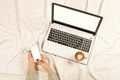 Woman using smart phone on her bed. Woman working on laptop and drink cappuccino coffee at home in the morning top view. Lifestyle