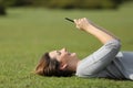 Woman using a smart phone resting on the grass in a park Royalty Free Stock Photo