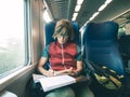 Woman using smart phone sitting traveling by train hand writing on paper. Desaturated cold tone color grading. Working mobility co Royalty Free Stock Photo