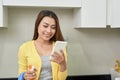 Woman using smartphone while cleaning the kitchen Royalty Free Stock Photo