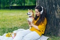 Woman using smartphone listening to music in headphones in green park with dog Royalty Free Stock Photo