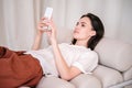 Woman using smartphone, relaxing on beige sofa at home Royalty Free Stock Photo