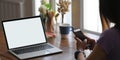 A woman is using a smartphone while sitting in front of a white blank screen computer laptop Royalty Free Stock Photo