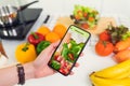 Woman using smartphone and touching application screen for ordering salad online on the table at the kitchen. Royalty Free Stock Photo