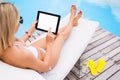 Woman using tablet computer while sunbathing in chair by the pool