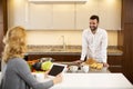 Woman using tablet at the kitchen table while man preparing food Royalty Free Stock Photo