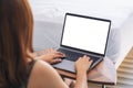 A woman using and typing on laptop with blank white desktop screen keyboard on wooden table next to the bed Royalty Free Stock Photo