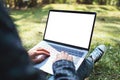A woman using and typing on laptop with blank white screen , sitting in the outdoors with nature background Royalty Free Stock Photo