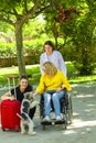 Woman using a wheelchair and another woman with a suitcase pet a cheerful dog at a park Royalty Free Stock Photo