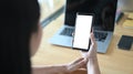 A woman is using a white blank screen mobile phone while sitting in front of a computer laptop. Royalty Free Stock Photo