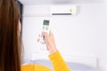 Woman is using white remote of air conditioner for turn on or adjust temperature of air conditioner inside the room