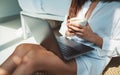 A woman using and working on laptop computer while drinking coffee and sitting in bedroom at home Royalty Free Stock Photo