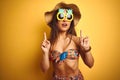 Woman on vacation wearing bikini and pineapple sunglasses over isolated yellow background amazed and surprised looking up and Royalty Free Stock Photo