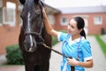 Woman veterinary doctor holding thoroughbred horse by bridle in stable and stroking head Royalty Free Stock Photo