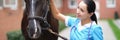 Woman veterinary doctor holding thoroughbred horse by bridle in stable and stroking head Royalty Free Stock Photo