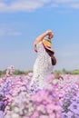 A Woman In A Vintage Dress Stretch Oneself Out In Purple Flower Field In The Morning After Waking Up. Young Tourists Strolling