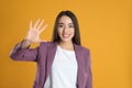 Woman in violet blazer showing number five with her hand on yellow background Royalty Free Stock Photo