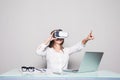 Woman in VR glasses. Confident young woman in virtual reality headset pointing in the air while sitting at her working place in of