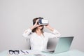 Woman in VR glasses. Confident young woman in virtual reality headset pointing in the air while sitting at her working place in of