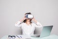 Woman in VR glasses. Confident young woman in virtual reality headset pointing in the air while sitting at her working place in of