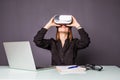 Woman in VR glasses. Confident young woman in virtual reality headset pointing in the air while sitting at her working place in of