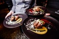 Woman waiter carries three plates of food. Meat steak garnished with two sauces on a dark plate Royalty Free Stock Photo