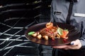 Woman waiter holding a dark round plate with grilled juicy steak with grilled mushrooms, tomatoes and cranberries. Royalty Free Stock Photo