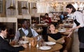 Woman waiter is taking order from smiling company in hall