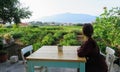 A woman waiting at a table ready to enjoy a meal with a view of a sprawling wine vineyard growing the local grk grapes