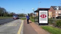 A woman waits for an approaching bus at a bus stop with a HSBC British Cycling post on the side