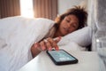 Woman Waking Up In Bed Reaches Out To Turn Off Alarm On Mobile Phone Royalty Free Stock Photo