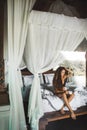 Woman waking up and enjoying morning coffee in bed with white canopy.