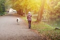 Woman walk with dog in park path, talking by phone.