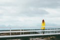 Woman walking alone on bridge Travel Lifestyle emotional concept vacations outdoor yellow raincoat clothing foggy mountains Royalty Free Stock Photo